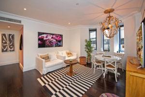 Feature light fitting, timber chandelier, black and white rug, large art pieces, interesting furniture, large TV Eclectic open concept living room in Sydney with white walls, dark hardwood floors and a freestanding tv.