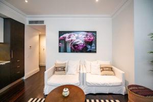 Flower art, white couches, black and white rug, antique coffee table, afghan foot stools Eclectic living room in Sydney with white walls, dark hardwood floors and a freestanding tv.