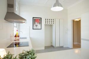 Design ideas for a small contemporary l-shaped separate kitchen in Sydney with a double-bowl sink, flat-panel cabinets, white cabinets, solid surface benchtops, white splashback, porcelain splashback, stainless steel appliances, laminate floors, no island and grey floor.