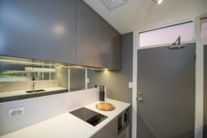 Design ideas for a small contemporary galley separate kitchen in Sydney with a single-bowl sink, flat-panel cabinets, solid surface benchtops, mirror splashback, light hardwood floors and no island.