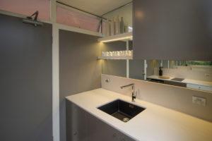 Design ideas for a small contemporary galley separate kitchen in Sydney with a single-bowl sink, flat-panel cabinets, solid surface benchtops, mirror splashback, light hardwood floors and no island.