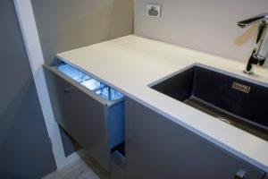 Small contemporary galley separate kitchen in Sydney with a single-bowl sink, flat-panel cabinets, solid surface benchtops, mirror splashback, light hardwood floors and no island.