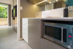 Inspiration for a small contemporary galley separate kitchen in Sydney with a single-bowl sink, flat-panel cabinets, solid surface benchtops, mirror splashback, light hardwood floors and no island.