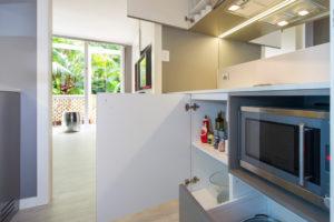Inspiration for a small contemporary galley separate kitchen in Sydney with a single-bowl sink, flat-panel cabinets, solid surface benchtops, mirror splashback, light hardwood floors and no island.