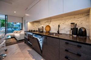Inspiration for a mid-sized contemporary single-wall open plan kitchen in Sydney with an undermount sink, flat-panel cabinets, white cabinets, marble benchtops, white splashback, marble splashback, stainless steel appliances, light hardwood floors and with island.